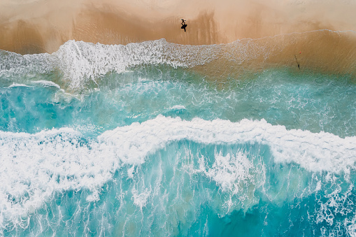 Surfer on tropical beach with blue transparent ocean and waves. Aerial view