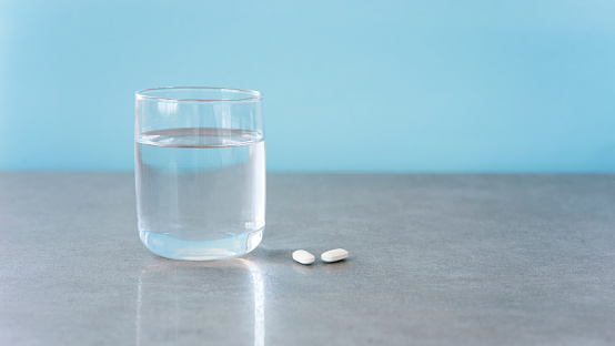 White medical pills and a glass of water on a light blue background, copy the space. The concept of medicine and Pharmacy