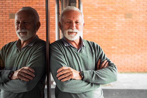 Mature man leaning on glass wall posing