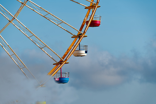 Superb photo of a Ferris wheel lost in the clouds, the colorful nacelles disappear behind the clouds