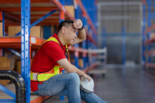 Tired stress Asian male worker labor hard working fatigue sitting resting in warehouse cargo inventory industry.