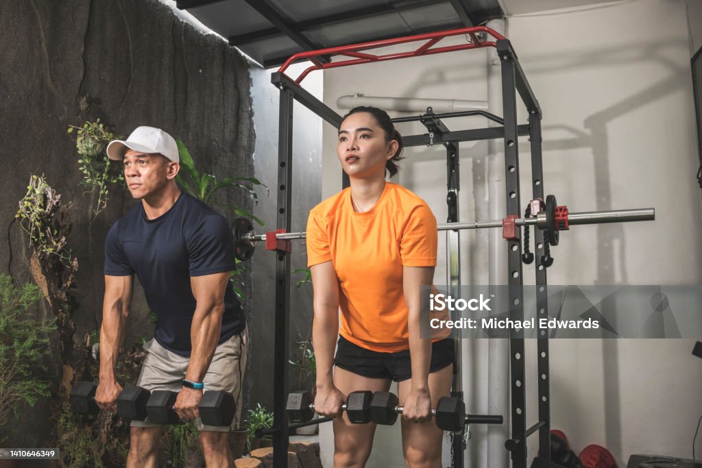 A man and woman simultaneously doing a set of Romanian deadlifts. Couple working out at a home gym. Exercising Stock Photo