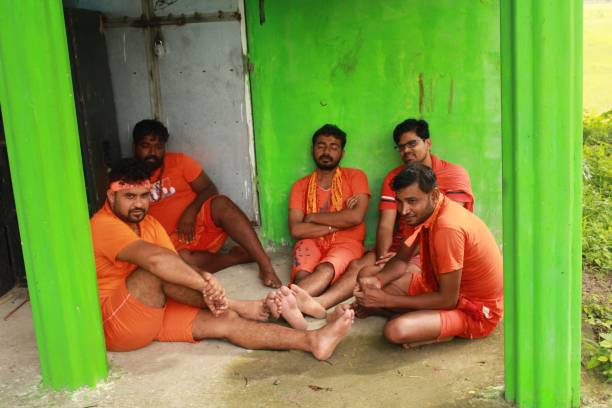 Shravan, commonly called Sawan, is the fourth Hindu month per the Lunar calendar. Dedicated to Lord Shiva, this month marks the beginning of the holy Chaturmas period.The 2022 Kanwar yatra begins on July 14, Thursday. Jal abhishekam is on Sawan shivaratri which falls on July 18. Moreover, the season of regional and pan India festivals,The festivals run during the monsoon month Shraawan (July — August). After taking water from the Ganges river (or other nearby river that wind up in the Ganges) the pilgrims, known as kanwariya or Shiv Bhaktas (disciples of Shiva), are mandated to travel barefooted and in saffron robes with their Kanwar (walking sticks used to hang the urns of water) for 105 km by various routes and usually in groups made of family, friends and or neighbors, and return to their own local or other more prestigious and larger Shiva Temples to pour Gangajal on Lord Shiva (Shiv Linga). On the march pilgrims continuously sprinkle any and all talk with 18 de julio de 2022 - sawan somwar vrat, kanwar yatra, kavaḍ yatra o kawad yatra. grupo de devotos hindúes de esperar cerca del templo local de shiv para realizar el kanwar yatra anual con agua sagrada del ganges para jal abhishekam del señor shivling.
