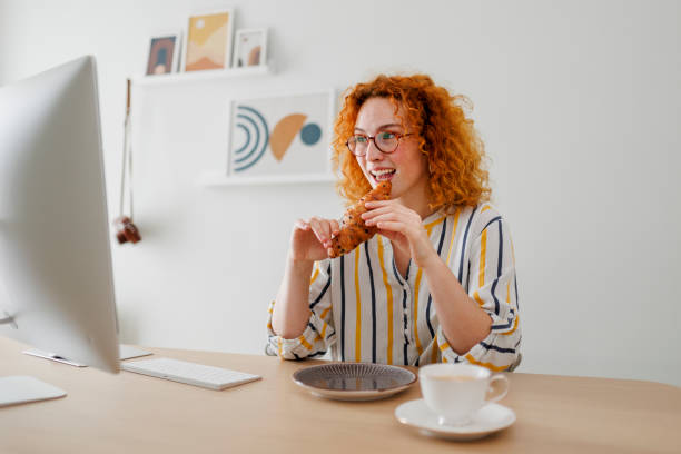 istock Woman eating croissant while working at office 1410650098