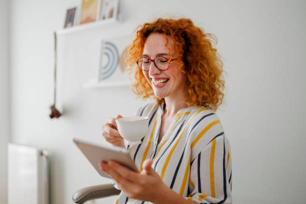 istock Redhead woman using digital tablet and drinking coffee at the office 1410650233