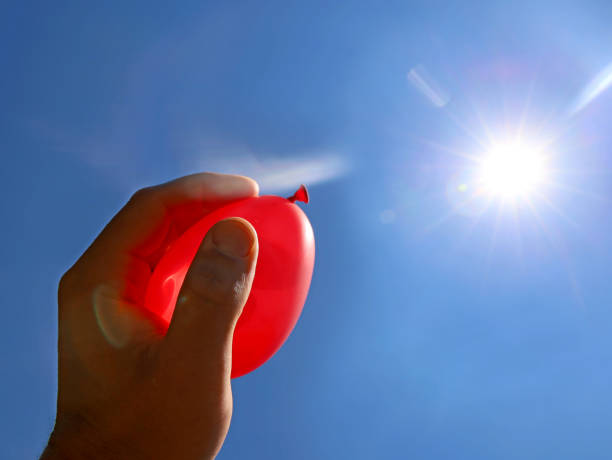 hand holds red water balloon against the summer sun, water bomb ready for cooling down attack hand holds red water balloon against the summer sun, water bomb ready for cooling down attack. water balloon stock pictures, royalty-free photos & images
