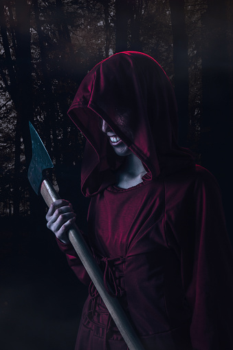 Disguised person in red dress holding an axe in the dark forest.