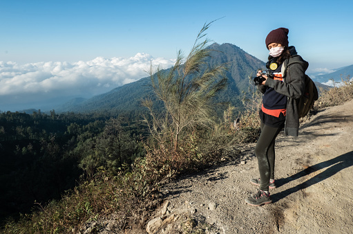 Female landscape photographer hiking on mountain or volcano and taking photographs of the valley from view point