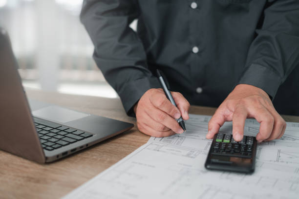 istock Engineering work concept: Close up hand a use pen mark CAD drawing and calculator in Calculating document and laptop on the wood table in office 1410655215