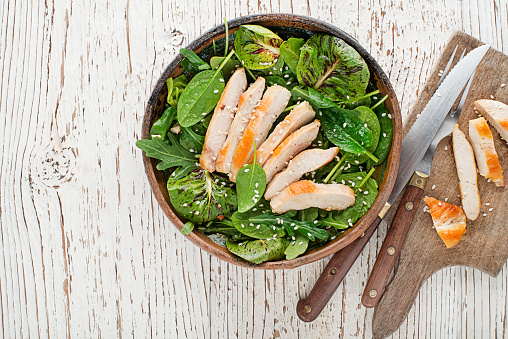 Healthy green salad with chicken breast on wooden table background