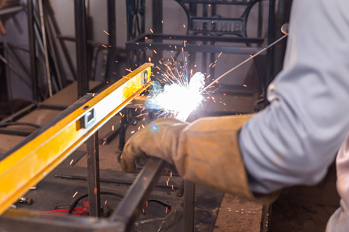 Welding the corner joint of a steel frame. Using a level bar to check balance. Fabricating custom furniture at a workshop or factory.