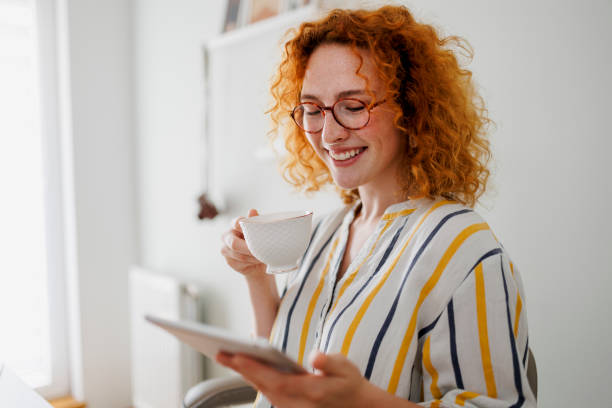 istock Redhead woman using digital tablet and drinking coffee at the office 1410657847