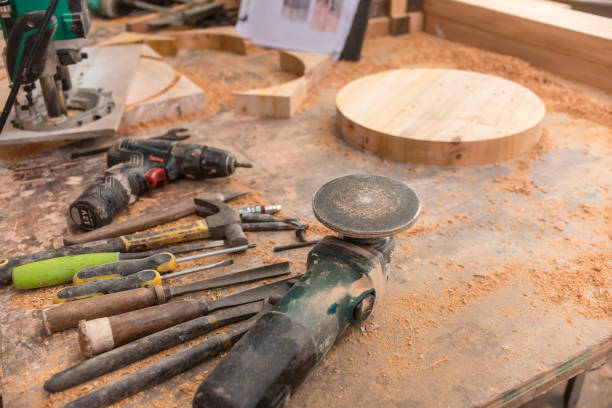 istock Woodworking tools on a table filled with sawdust. Drills, a hammer, screwdrivers, chisels and an angle grinder. A finished circle slab with reference drawing for a stool design at the back. 1410657920