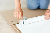 Woman hand screwing screw in white plank. Using hex key. Assembling new furniture. Closeup.