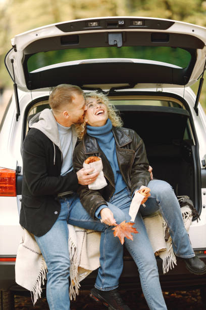 Romantic couple sitting in a trunk of white car in a forest and hugging stock photo