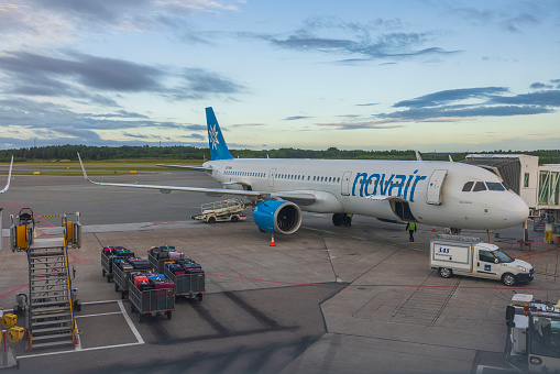 Sweden. Stockholm. 07.07.2022. Beautiful view of Novair aircraft parking lot at airport with baggage carts for loading against backdrop of early sunrise sky.