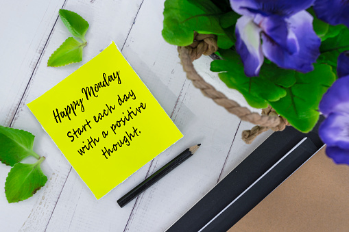 Motivational and inspirational quote on yellow note with flowers on wooden background - Happy monday, start each day with a positive thought.