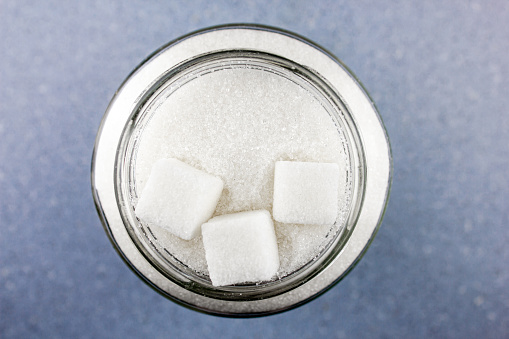 The Sugar in a glass jar.Pieces of sugar cubes and sugar crumbs.Sugar concept on a blue table top view.