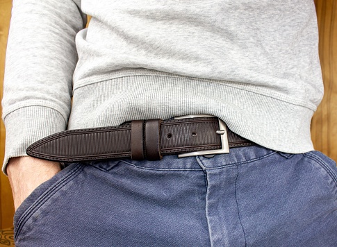 The man in trousers with a belt close-up. A young slender man in a white hoodie and jeans with a belt close-up anonymous.