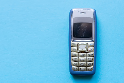 Old blue button mobile phone on blue background.