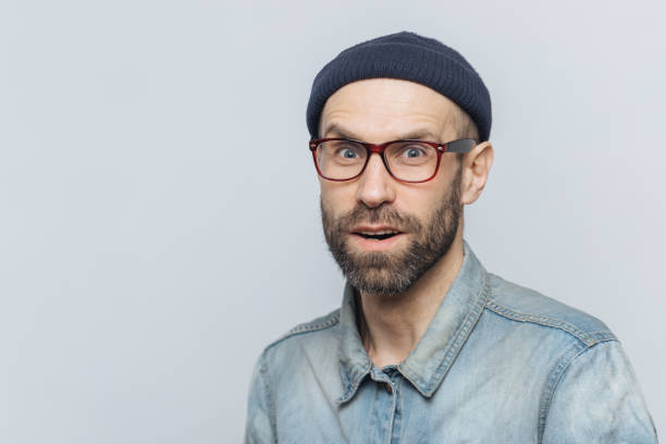 istock Stylish middle aged male with suprised and curious expression wears spectacles, denim jacket and hat, poses against grey background with copy space for your advertisment or promotional text. 1410673418
