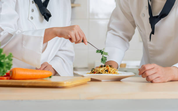 istock Selective focus, close up on hands of professional chefs wearing white uniform, decorating dish of spaghetti. Food, Hotel and Restaurant Concept. 1410674526
