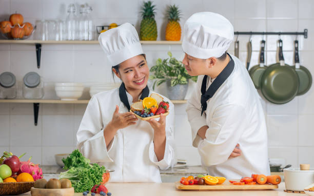 istock Two Asian professional couple chef wearing white uniform and hat, showing and testing breakfast meal, cooking in kitchen together, smiling with happiness, confidence. Food Concept. 1410674550