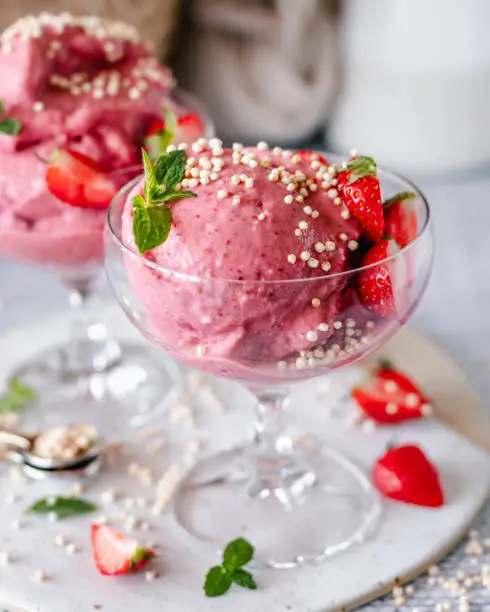 Close-up of a cup of homemade strawberry ice cream decorated with fresh strawberries, mint and puffed quinoa