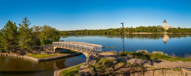 ruhiger wascana lake und die brücke entlang des wanderwegs des lake parks in regina, saskatchewan, kanada, mit blick auf das saskatchewan legislative building. - wascana lake stock-fotos und bilder