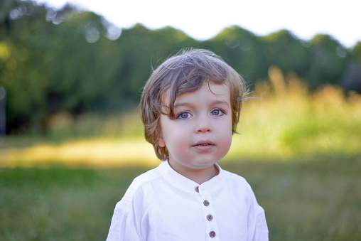Portrait of a little boy looking at camera with blank facial expression in a public park. Horizontal shot.