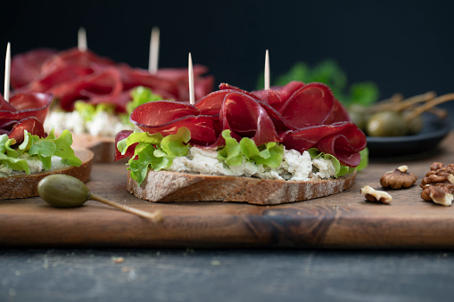 Tasty sandwich on a wooden cutting board, on a dark rustic wooden table, with cream and parsley, with a dark background, vertical image