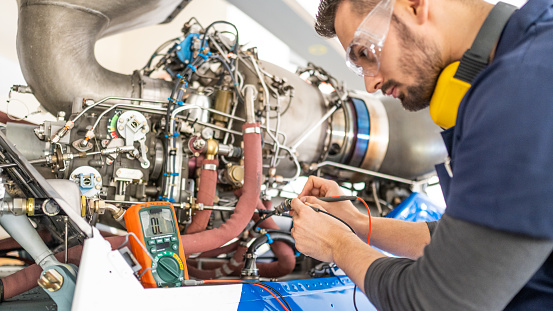 Aircraft engineer fixing jet engine and using multimeter, close up. Air vehicle mechanic examining helicopter, side view