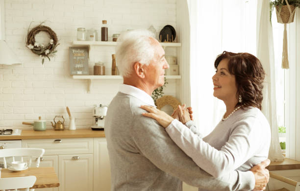 istock Happy charming elderly woman smiling at the camera while dancing waltz with her husband in the kitchen. 1410689567