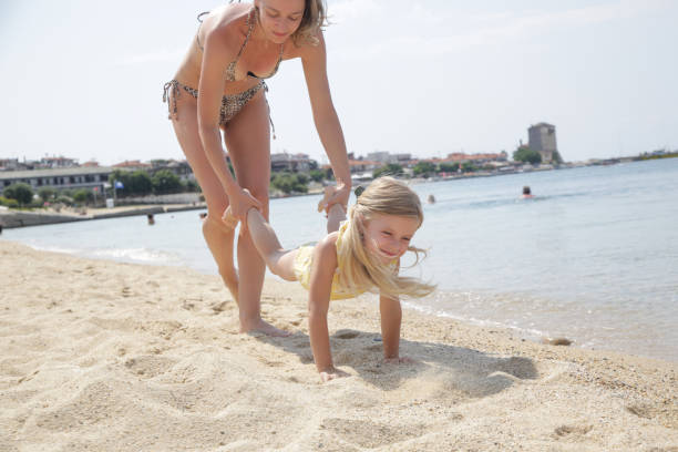 Mother and daughter playing on beach, exercising for a wheelbarrow race. Mother and daughter playing on beach, exercising for a wheelbarrow race. wheel barrow walks stock pictures, royalty-free photos & images