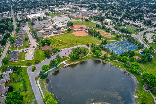 A drone view of a neighborhood sporting events venue between Dayton and Cincinnati Ohio. The complex features practice fields, soccer, baseball, and softball fields. There are basketball, pickle-ball and tennis courts.  There is a lap pool. There is a walking trail. There are parking lots. You can seen the surrounding housing and business developments.