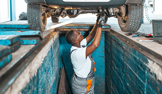 Auto repairman examining undercarriage of a car in a workshop.