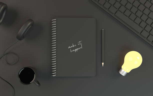 Make It Happen title is written on a gray notepad’s cover along with a turned on light build, headphones, computer keyboard and a full coffee cup with a black pencil on office table. Easy to crop for all your design and print needs.
