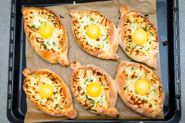 Adjarian khachapuri in the shape of a boat. Six portions on a baking tray as seen from above. A fluffy serving of hot khachapuri with a fatty egg yolk and two kinds of cheese. stock photo