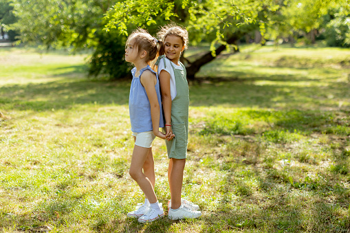 Two cute little girls standing back to back in the park