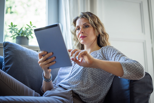 Woman at home, sitting on sofa and using digital tablet for trading online.