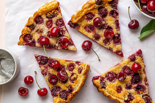 Slices of clafoutis with cherry on baking paper. Traditional homemade french cherry pie. Top view.