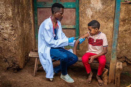 Male doctor vaccinating young African boy in small village, East Africa.