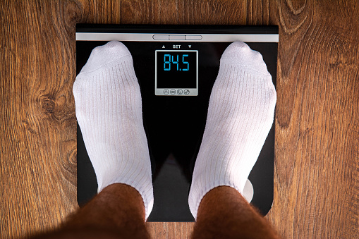 Weight loss. Man standing on digital scale after gym. Fitness life - man in white socks on black premium scale measuring himself after hard work. Man losing fat and calories. Obesity problems. Whey protein
