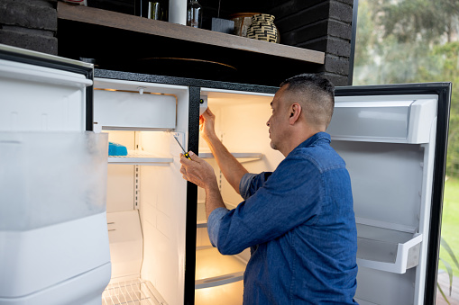 Latin American handyman fixing a fridge at a house - domestic life concepts