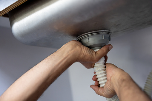 Close-up on a plumber fixing a pipe in the kitchen - domestic life concepts