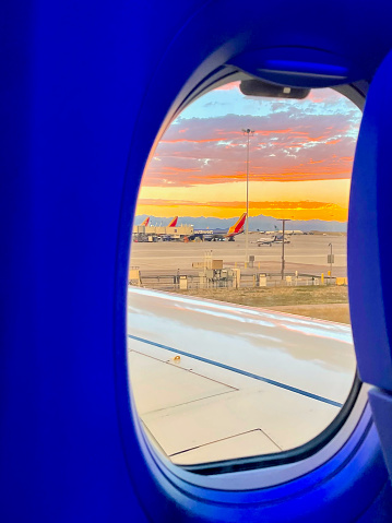 Denver, Colorado, USA - July 9, 2022: A deep-orange sunset over the Rocky Mountains is seen through the window of a Southwest Airlines Boeing 737-MAX8 aircraft taxiing toward the runway for an evening flight.