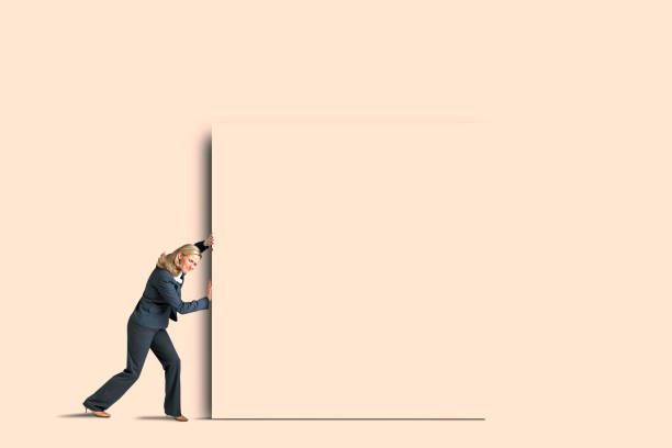 A businesswoman pushes a large beige block on a background of the same color