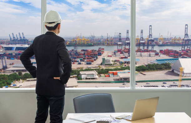Businessman standing at a port of its own, Back view of a young confident man financier is thinking about something, while is standing outdoors against sea port. stock photo