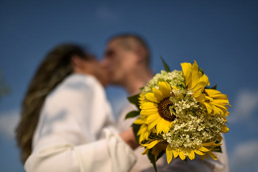 Photo of a defocused couple kissing each other and holding a bouquet of sunflowers