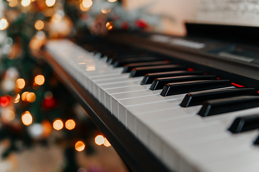 Piano keyboard with bright christmas lights on the background. Close-up shot of an a synthesizer with decorated background